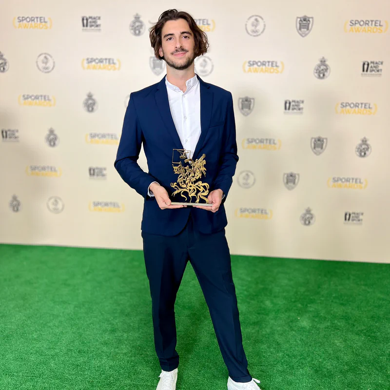 Thomas Gonçalves, son trophée doré en main, devant le mur des partenaires des Sportel Awards.